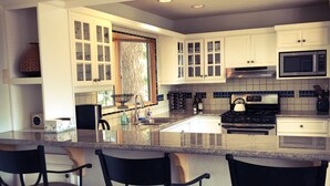 A modern kitchen with white cabinets, a large island with bar stools, a microwave, and a stove.