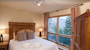A bedroom with a large bed, wooden headboard, two bedside tables with lamps, a window with curtains, and a wardrobe.
