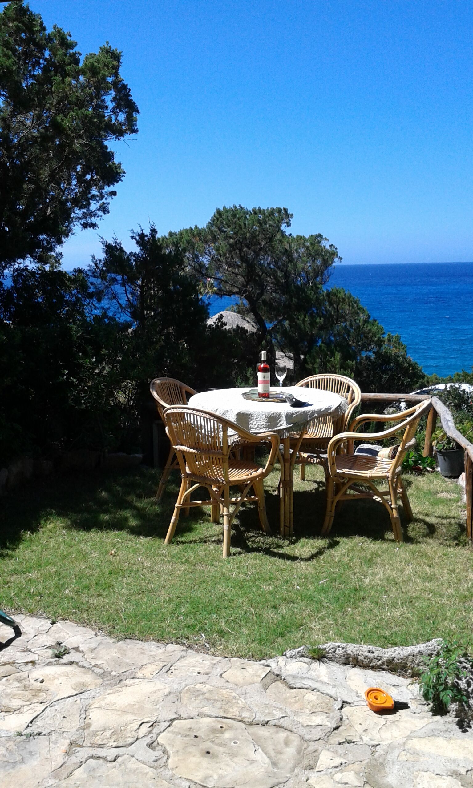 Un espacio de comedor al aire libre con sillas de mimbre y una mesa, con vista a un cuerpo de agua.