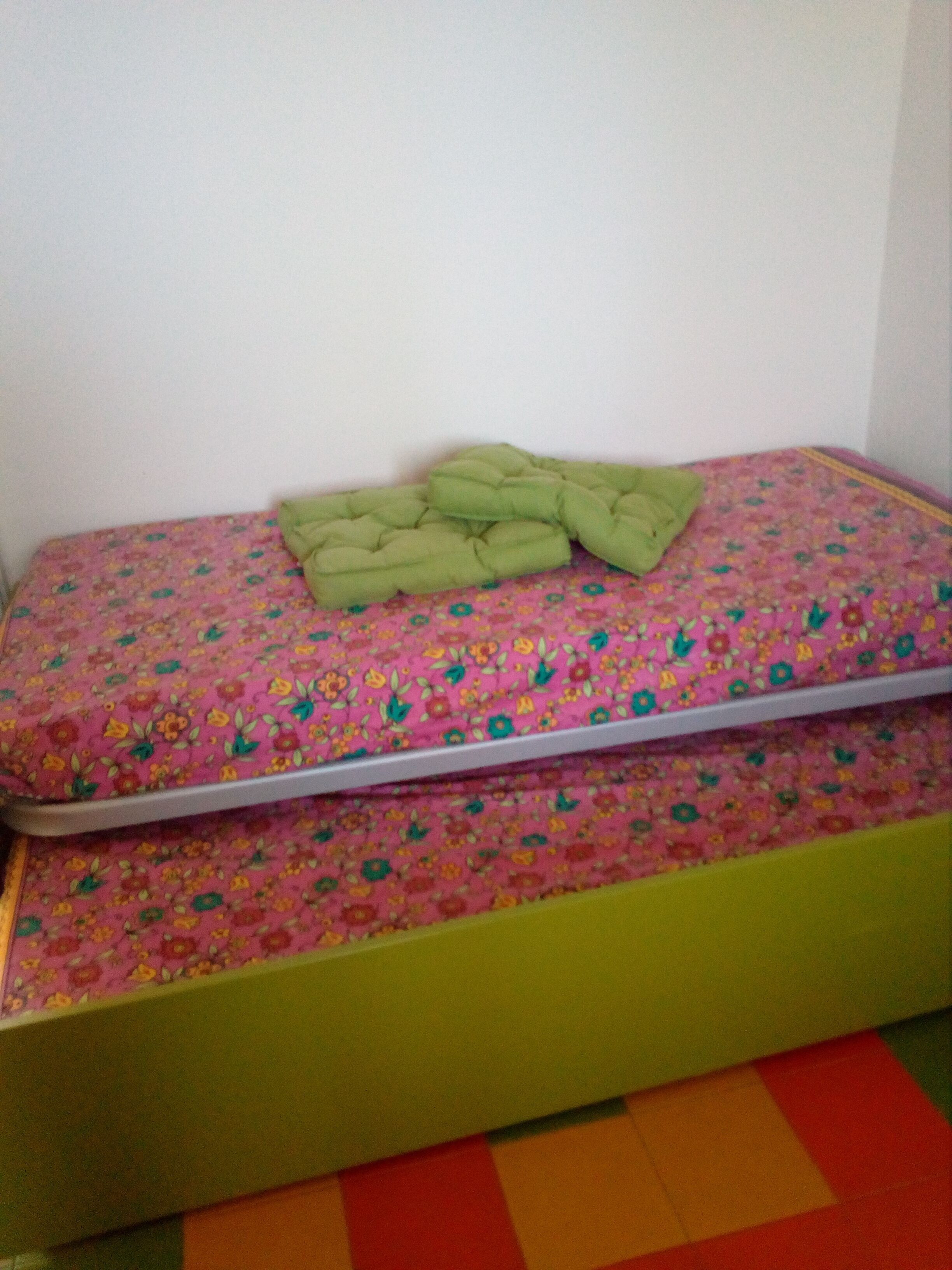 A small bed with a floral mattress cover and a green blanket.