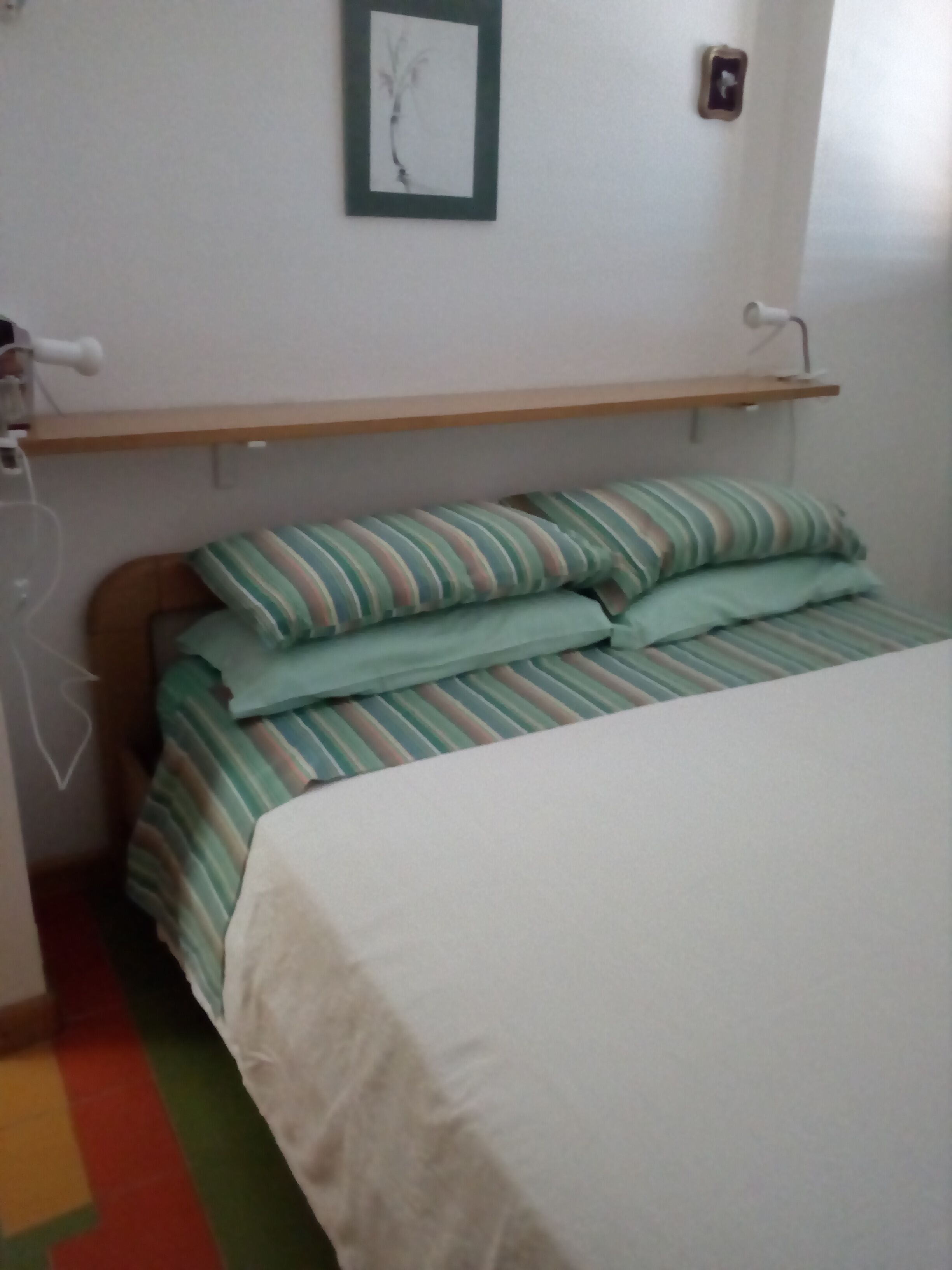 A bedroom with a bed, a bedside table, a shelf, and a wall-mounted picture.