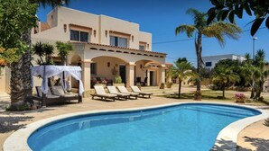 A pool area with lounge chairs and a building with arches and a tiled roof.