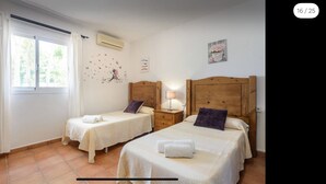 A bedroom with two beds, a window with curtains, an air conditioner, and a wall decoration.