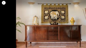 A wooden cabinet with drawers, a decorative tapestry with elephant motifs, a small lamp, and a vase on top.