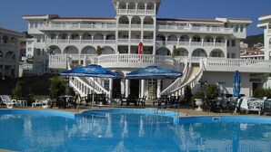 A large swimming pool with a white building in the background, featuring multiple balconies and a central staircase.