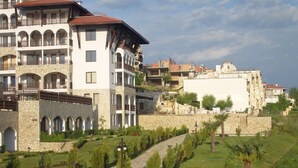 A multi-story hotel with stone facade, balconies, and a landscaped garden with pathways.