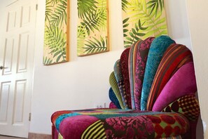 Una habitación con un sillón colorido, una puerta blanca y dos cuadros colgados en la pared.