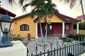 Ein Haus mit einer gefliesten Terrasse, einer Palme und einem Zaun.