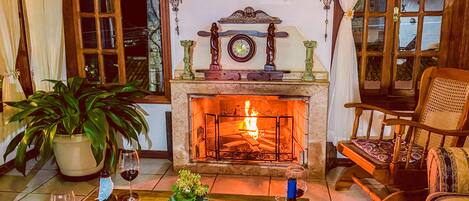 Un salón acogedor con chimenea, una mesa de comedor dispuesta con copas de vino y una botella, y un sillón cómodo.