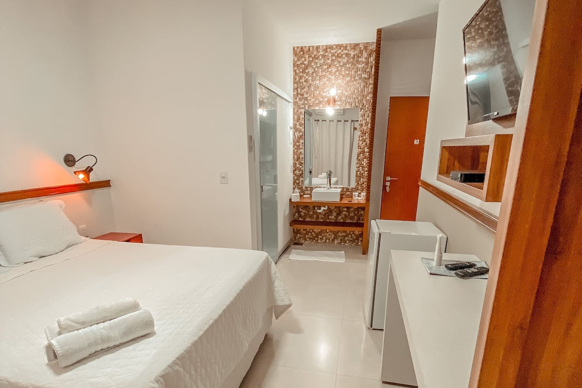 A hotel room with a bed, a desk, a mirror, and a shower area.
