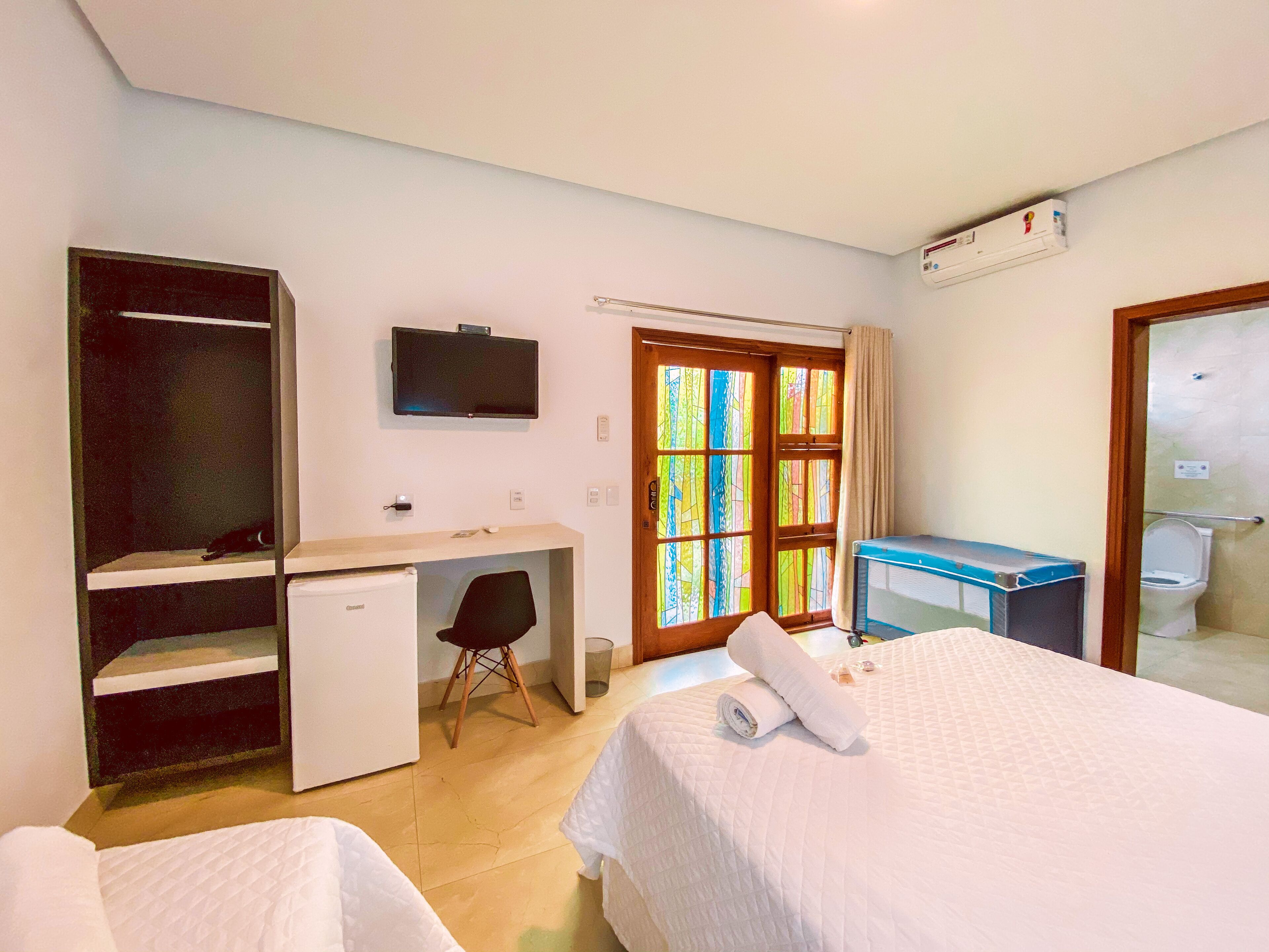 A hotel room with a bed, a desk, a chair, a TV, a wardrobe, and a bathroom.