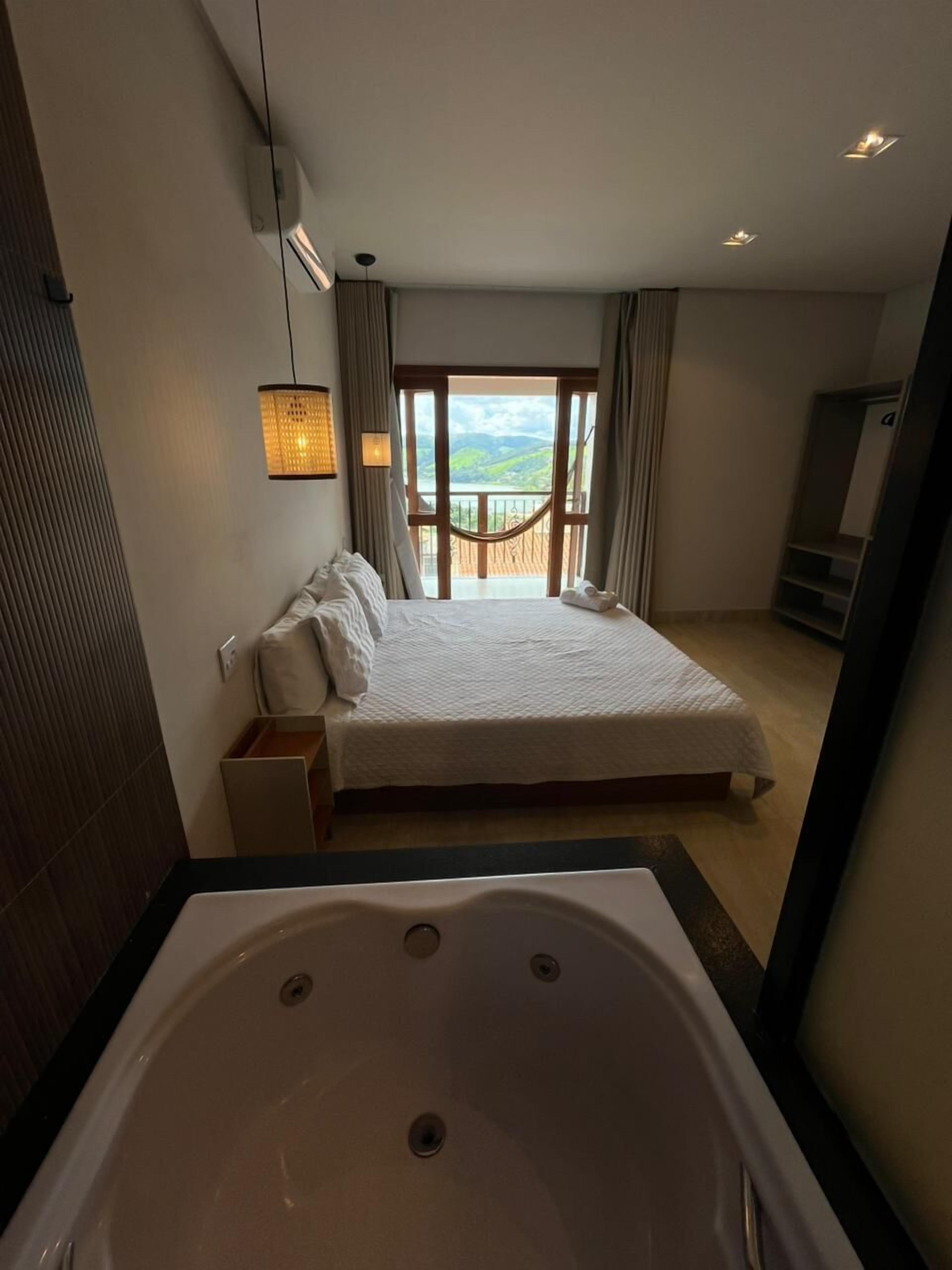 A hotel room with a large bed, a bathtub, a balcony with a view, and a TV.
