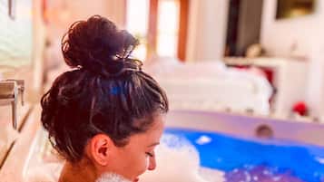 A person in a bathtub filled with bubbles, with a room in the background that includes a bed and a television.