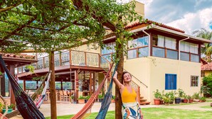 A person relaxing in a hammock in a lush garden area with a building in the background. - Pousada Quintal da Lua (Capitólio)