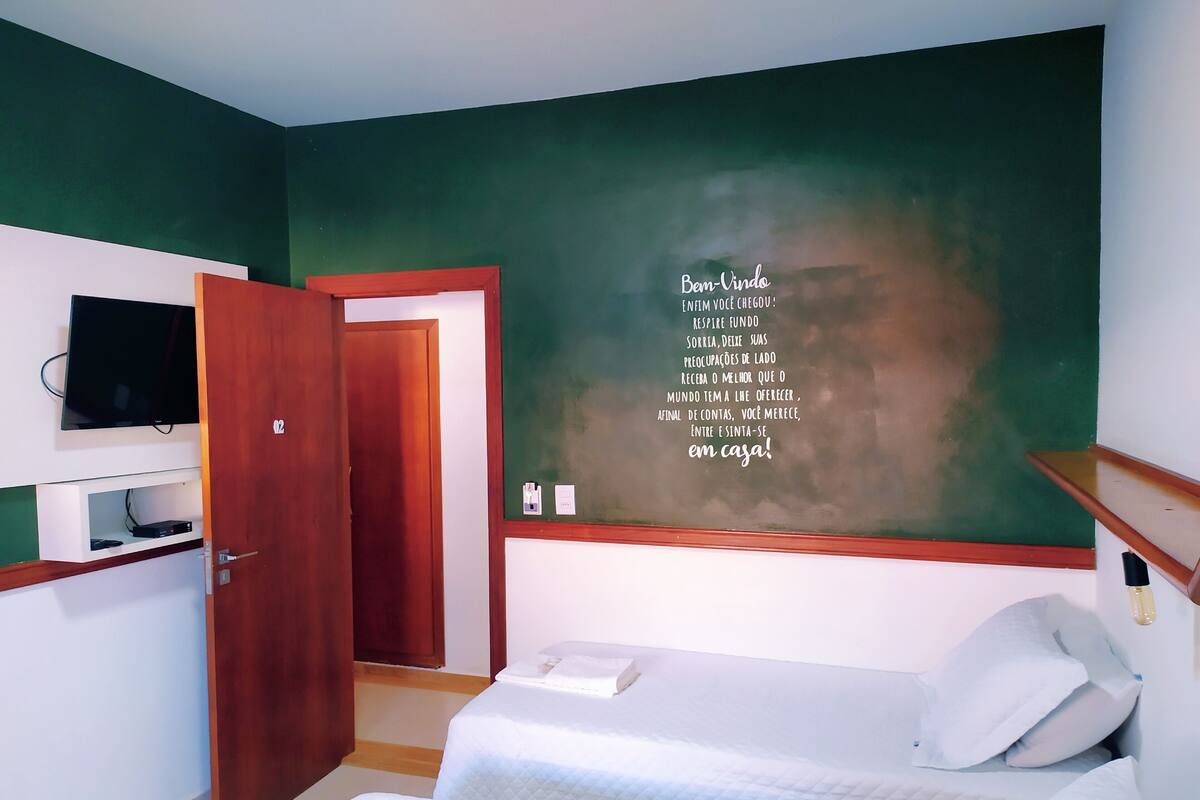 A hotel room with a bed, a television on a stand, a green wall, and a door.