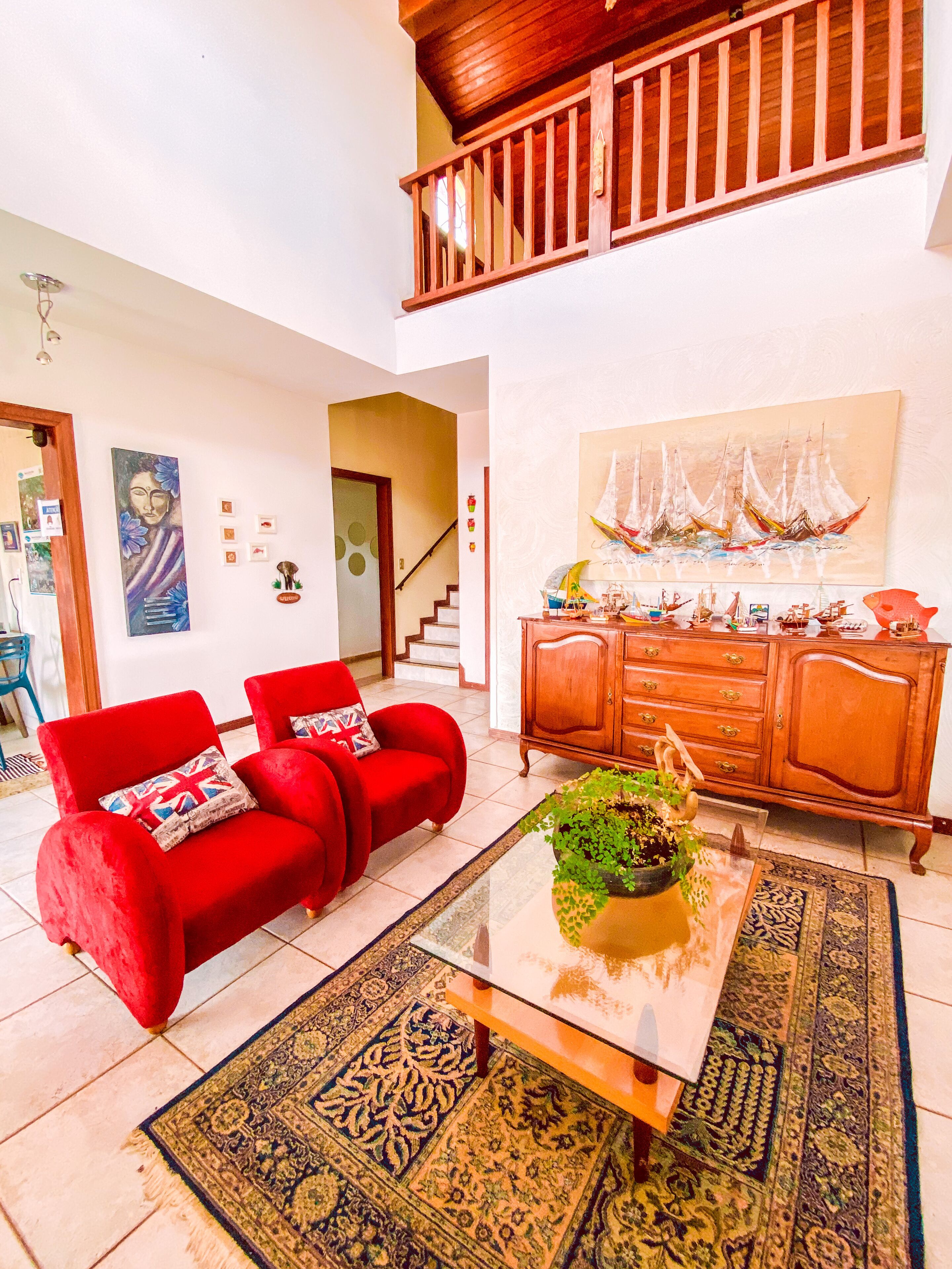 A spacious living room with a red sofa set, a wooden cabinet, and a large painting of sailboats.