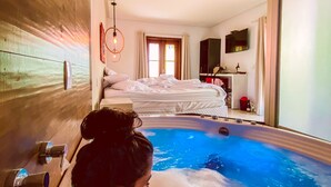 A room with a large bathtub, a bed, and a TV mounted on the wall. - Pousada Quintal da Lua (Capitólio)