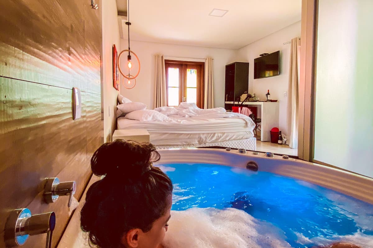 A room with a large bathtub, a bed, and a TV mounted on the wall.