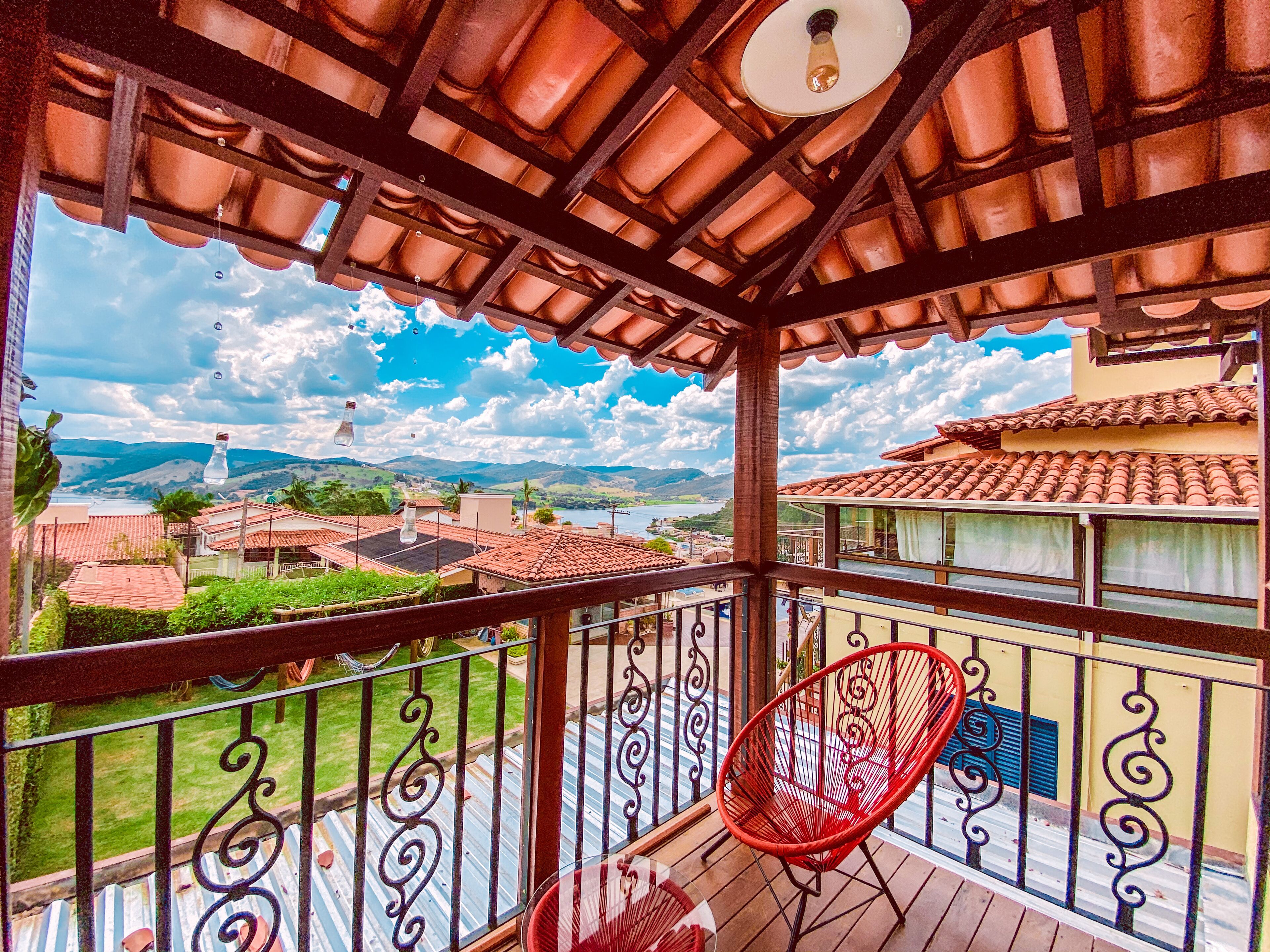 A balcony with a red chair, a view of a lake, and terracotta roofs.