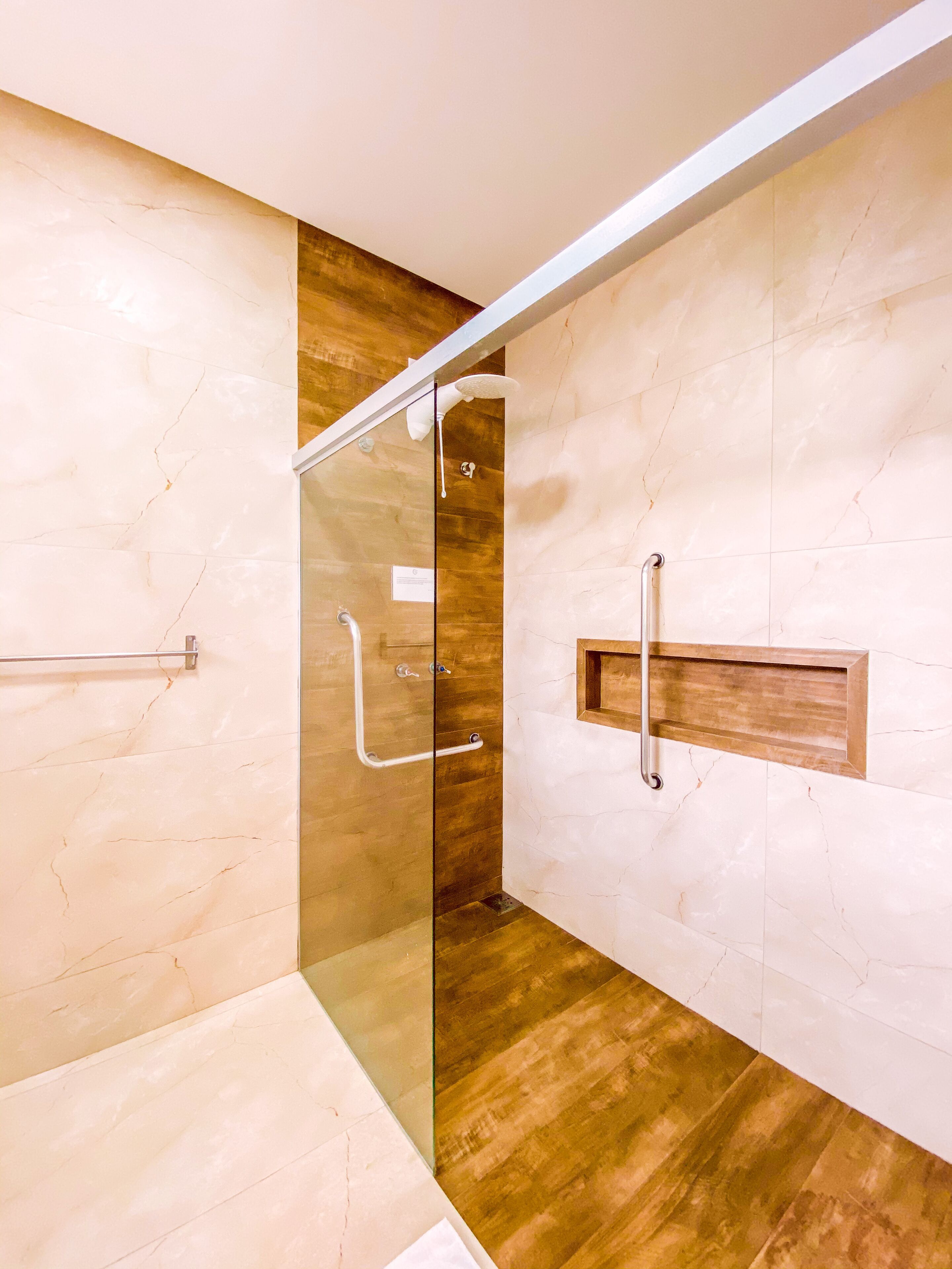 Un bagno moderno con cabina doccia in vetro, pavimento in legno e pareti in marmo.