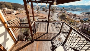 A wooden deck with a wrought iron railing, a wicker chair, and a view of a town and mountains. - Pousada Quintal da Lua (Capitólio)