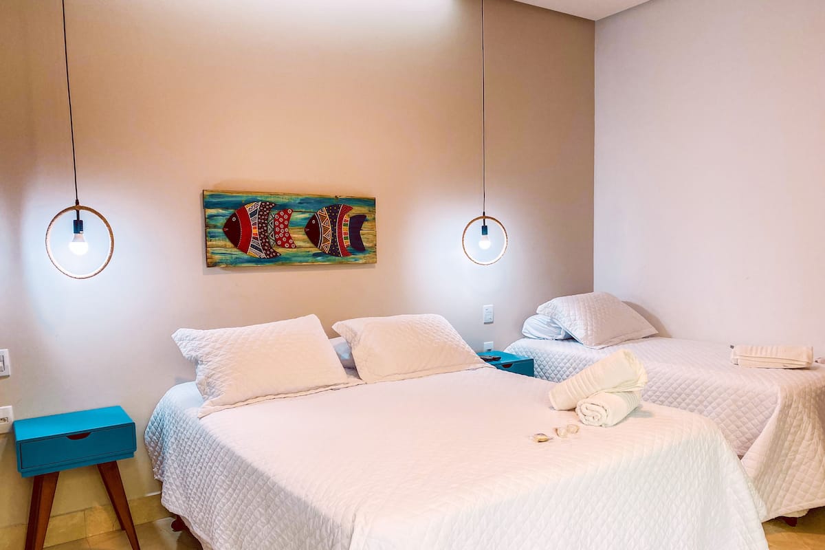 A hotel room with two beds, a blue nightstand, a painting on the wall, and two pendant lights.