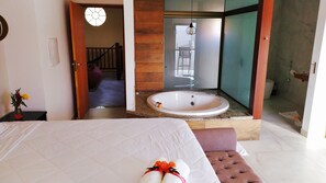 A hotel room with a large bed, a bathroom with a bathtub, and a view of the outside.