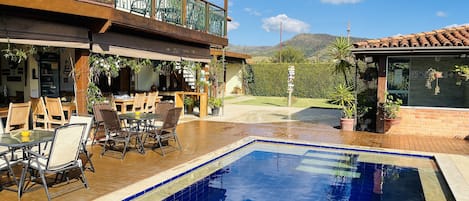 A pool area with a wooden deck, outdoor seating, and a view of the mountains.