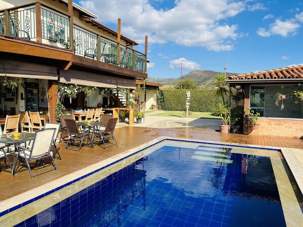 A pool area with a wooden deck, outdoor seating, and a view of the mountains.