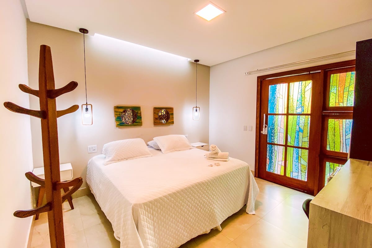 A bedroom with a bed, a wooden coat rack, two wall-mounted light fixtures, and a door with stained glass windows.