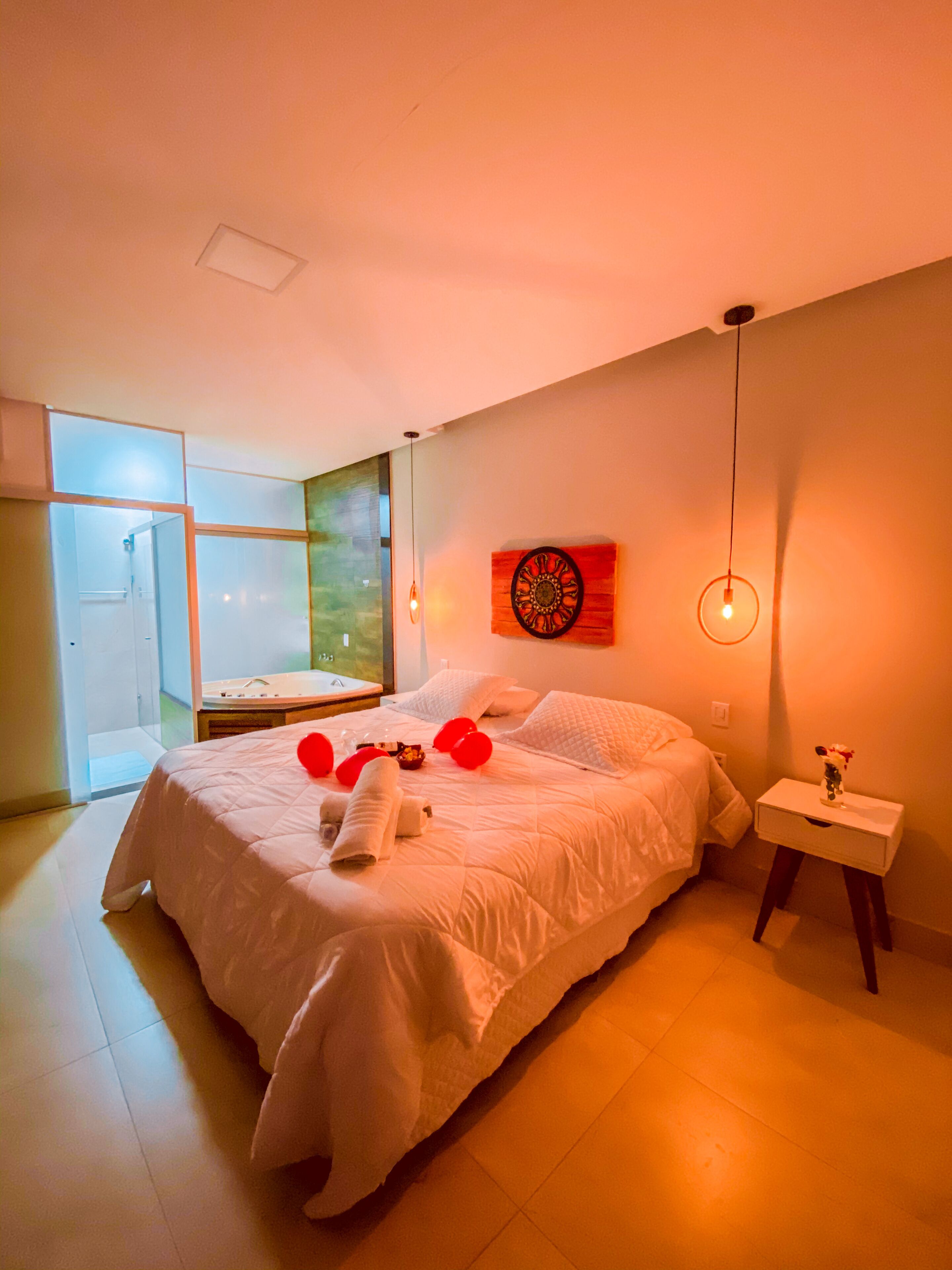 A modern bedroom with a large bed, a bedside table with a vase, and a window with a view.