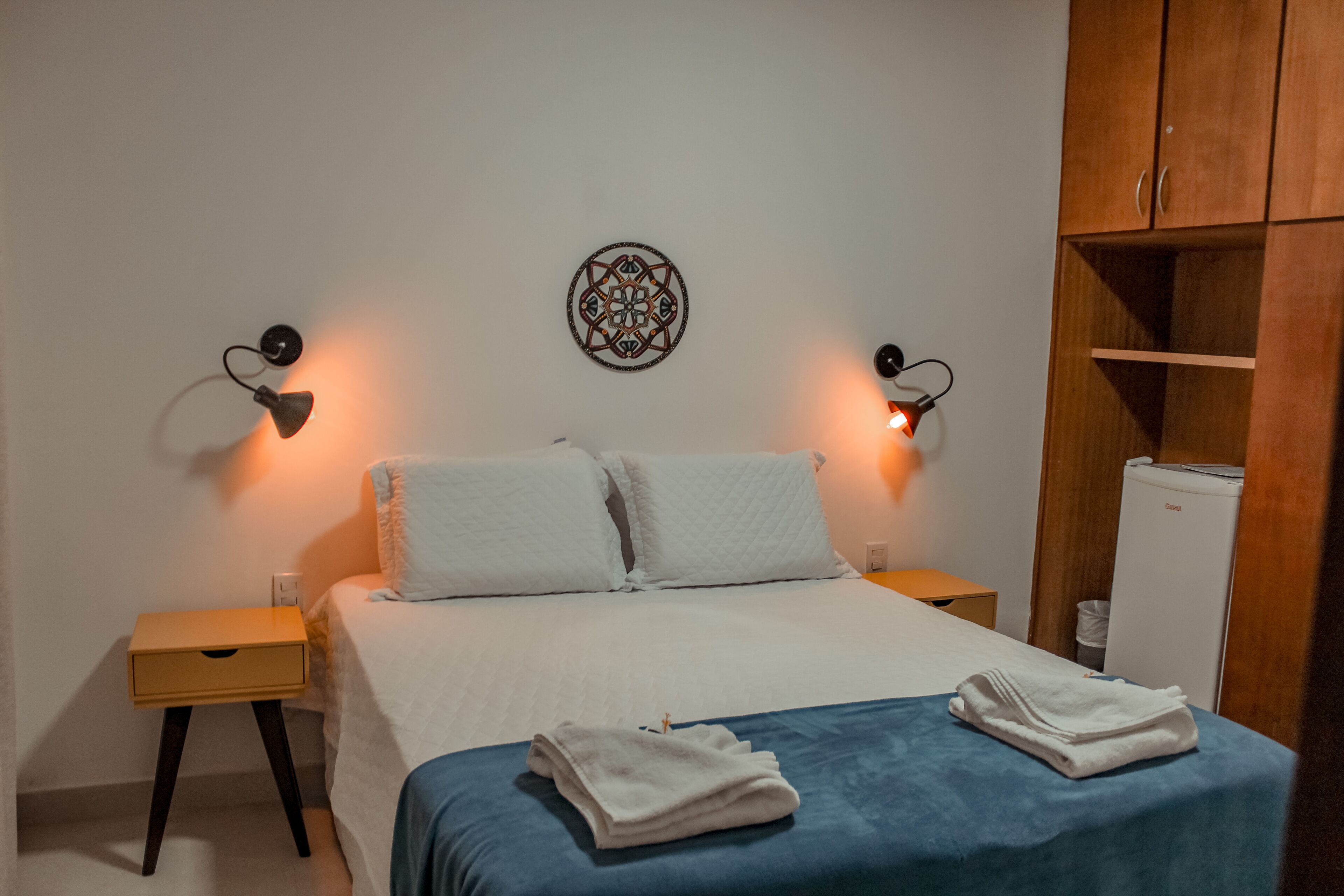 A bedroom with a bed, two nightstands, a wall decoration, and a wardrobe.