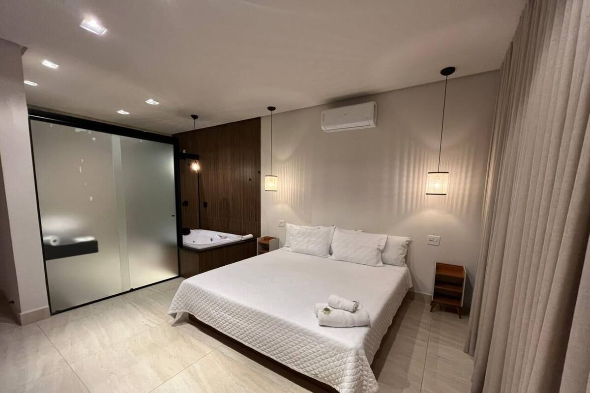 A modern bedroom with a large bed, a built-in wardrobe, a vanity with a mirror, and a small seating area.