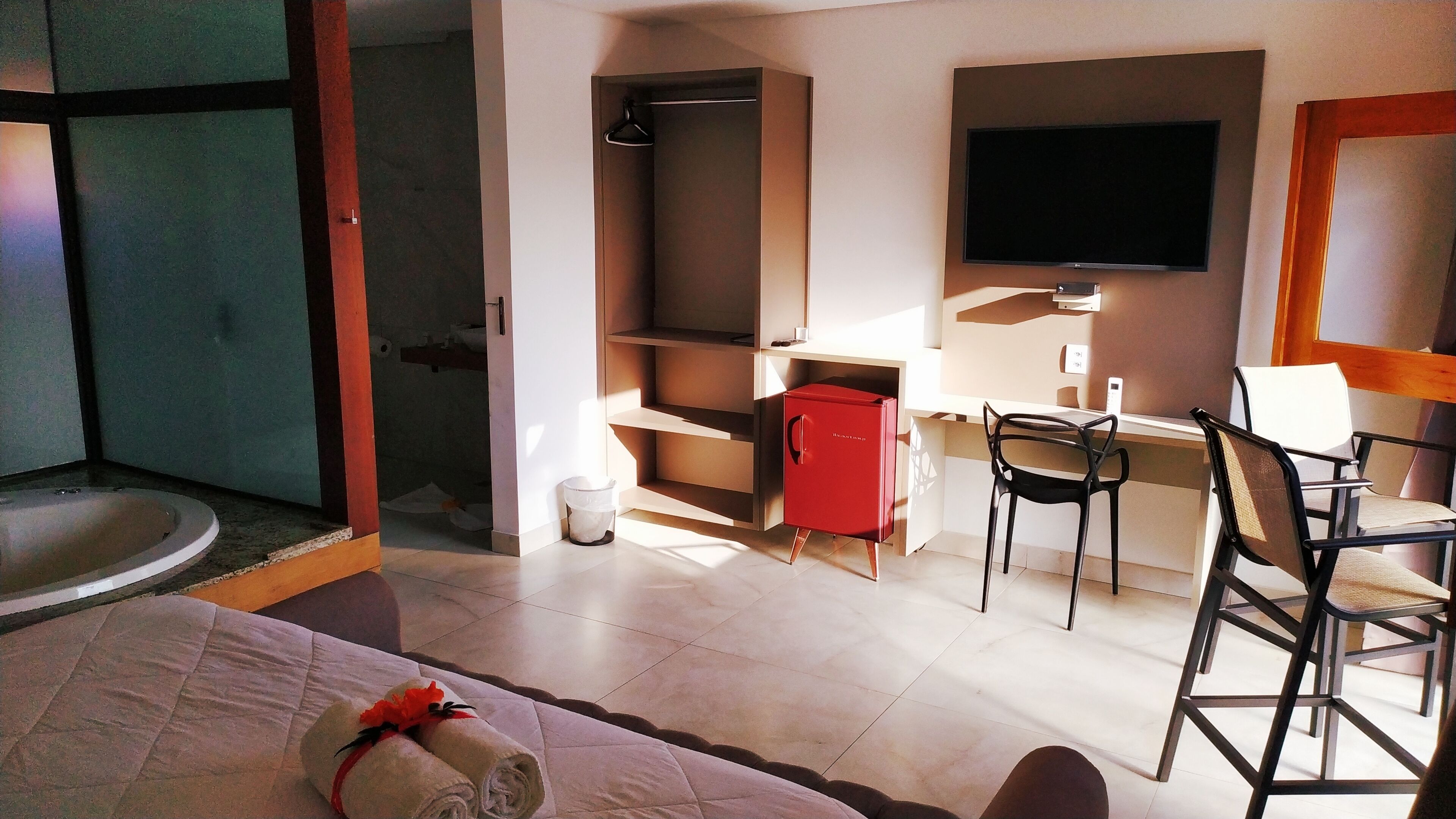 A hotel room with a bed, a desk with a chair, a television, and a red minibar.