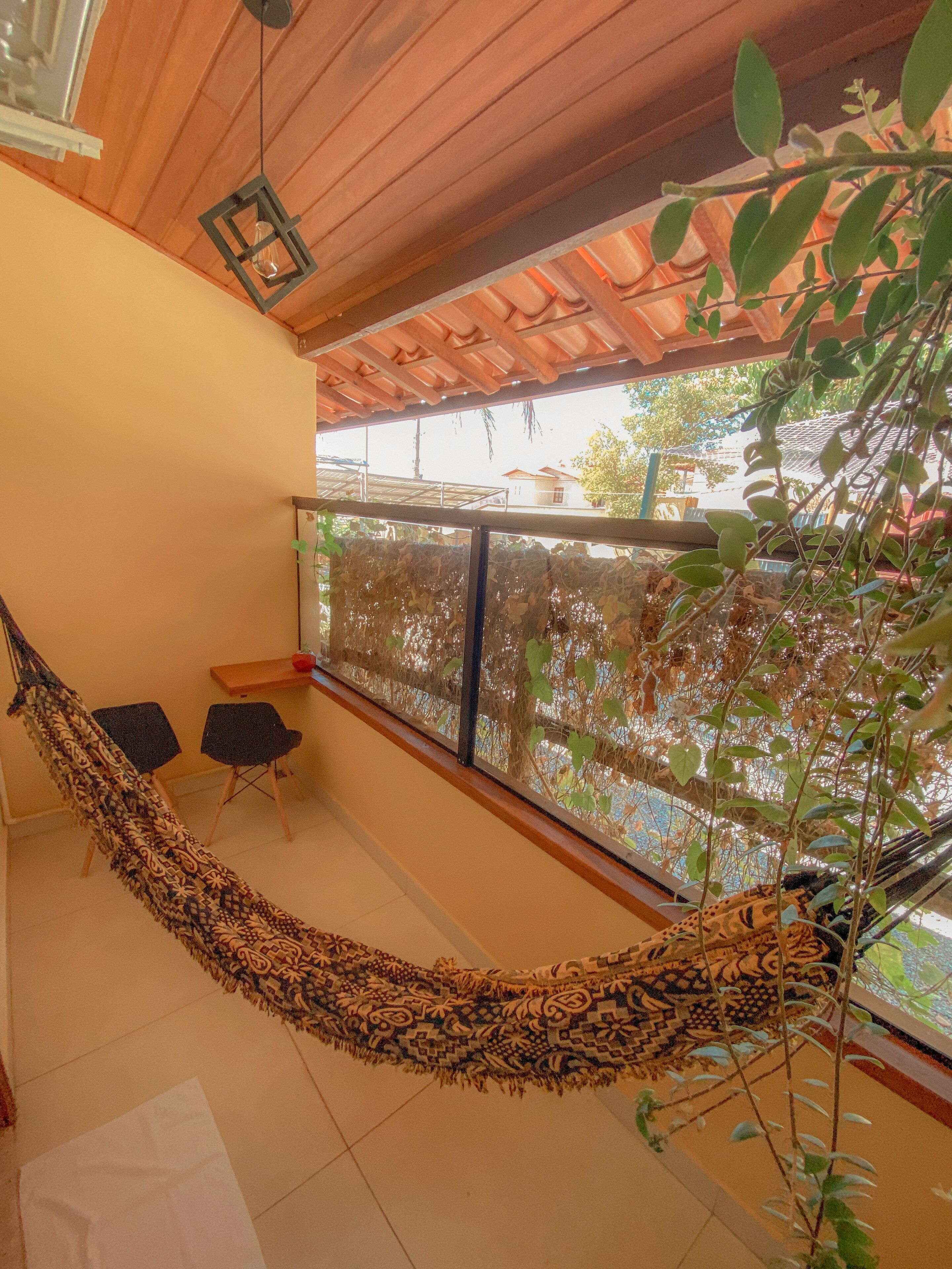 Una hamaca en una habitación con vistas a una casa y árboles. Hay dos sillas y una mesa.