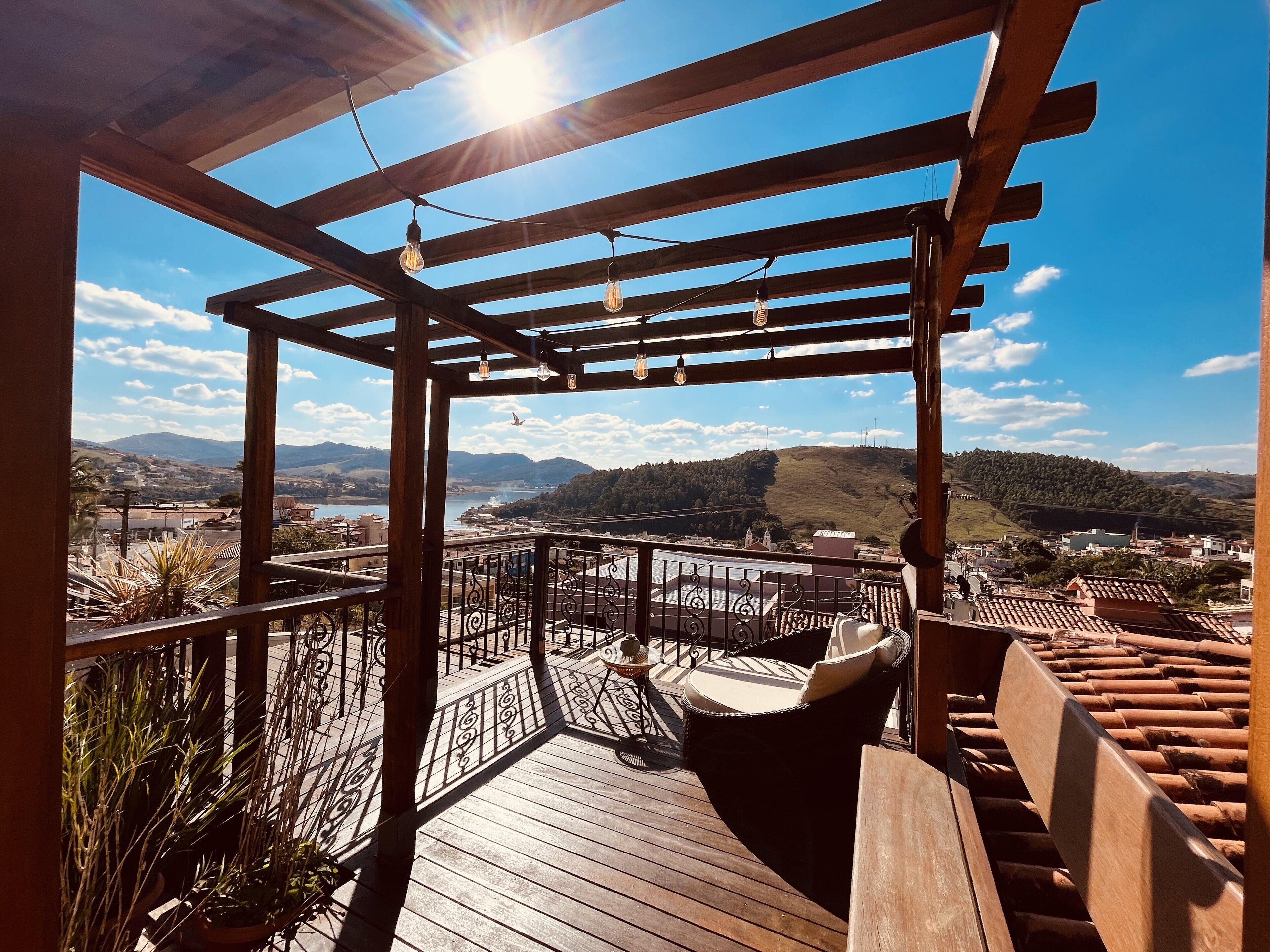 En træterrasse med pergola, udendørs møbler og udsigt over en dal og bjerge.