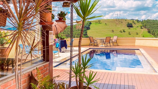 A pool area with a wooden deck, potted plants, and a view of a green landscape. - Pousada Quintal da Lua (Capitólio)