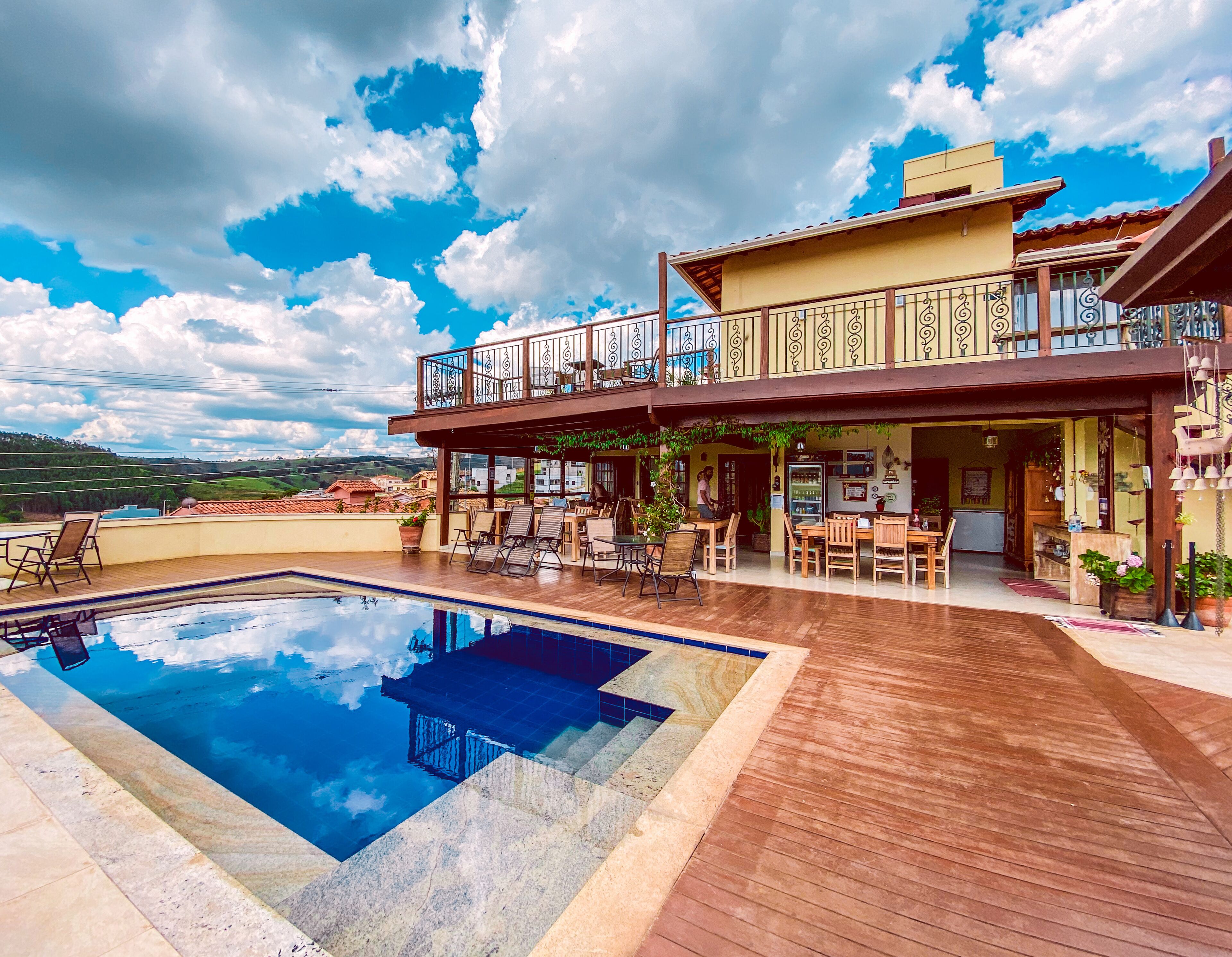 Un área de piscina en la azotea con terraza de madera, asientos al aire libre y vistas del paisaje circundante.