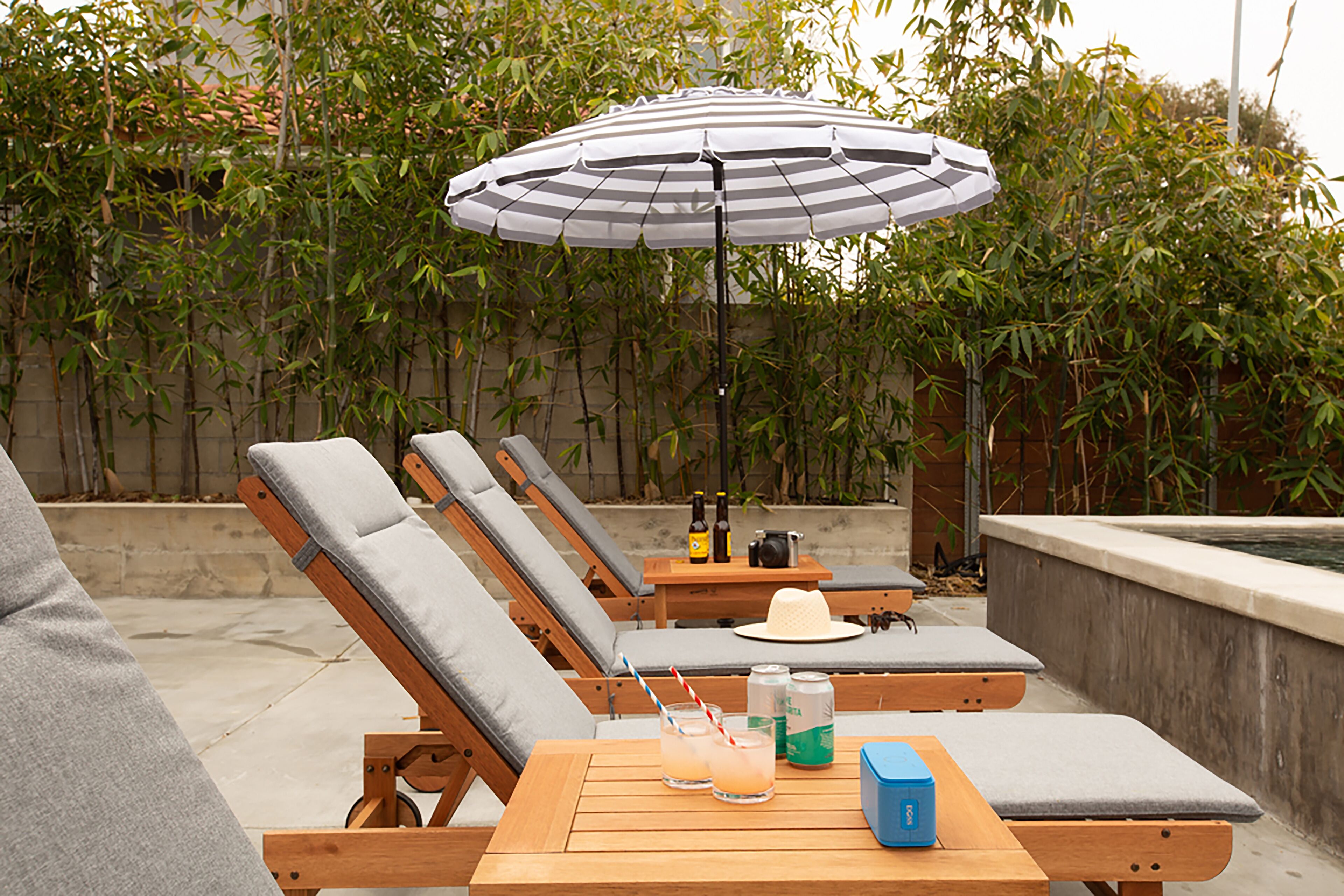 A poolside area with lounge chairs, a table with drinks, and an umbrella.