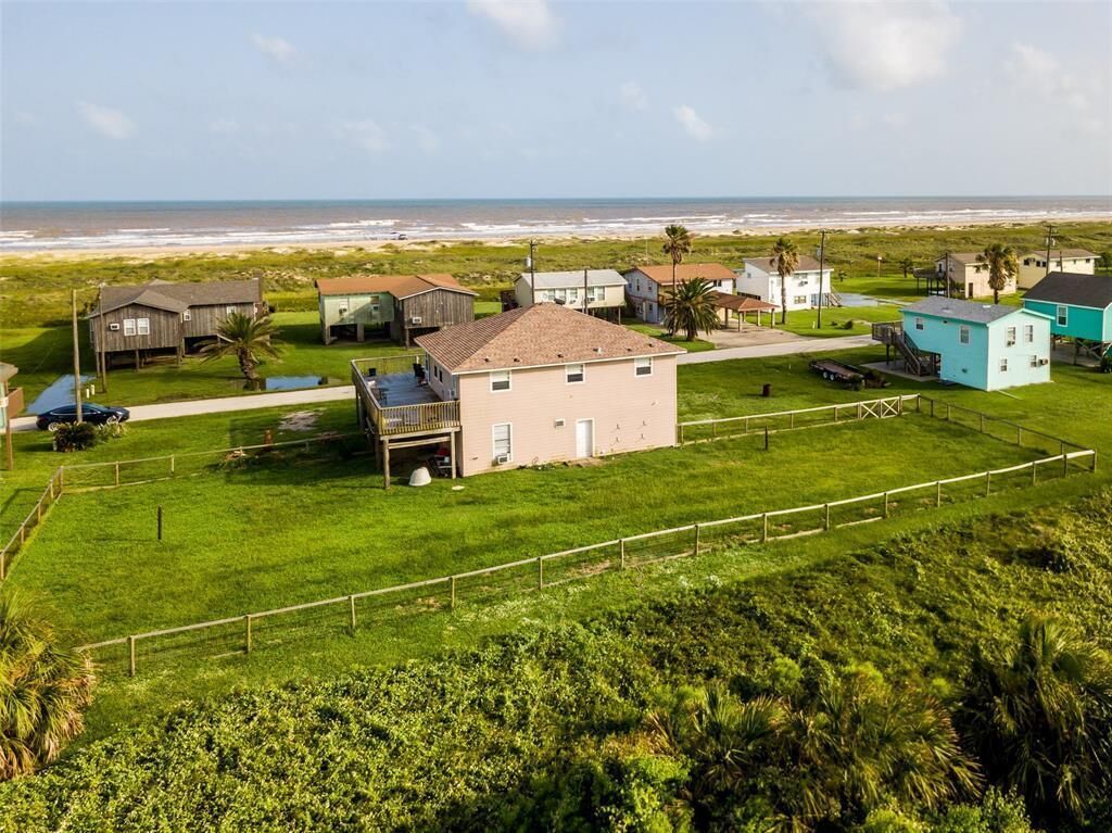 A coastal residential area with houses, a beach in the background, and a grassy field.