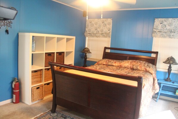 A bedroom with a wooden bed, a white shelving unit, wicker baskets, a lamp, and a fire extinguisher. - 💲Happy Beach Casa - View the Gulf (Matagorda)