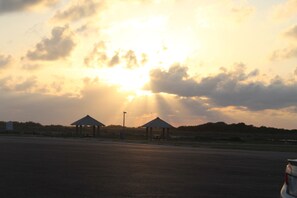 A parking lot with two small, open-sided structures, possibly gazebos, under a cloudy sky with the sun shining through.
