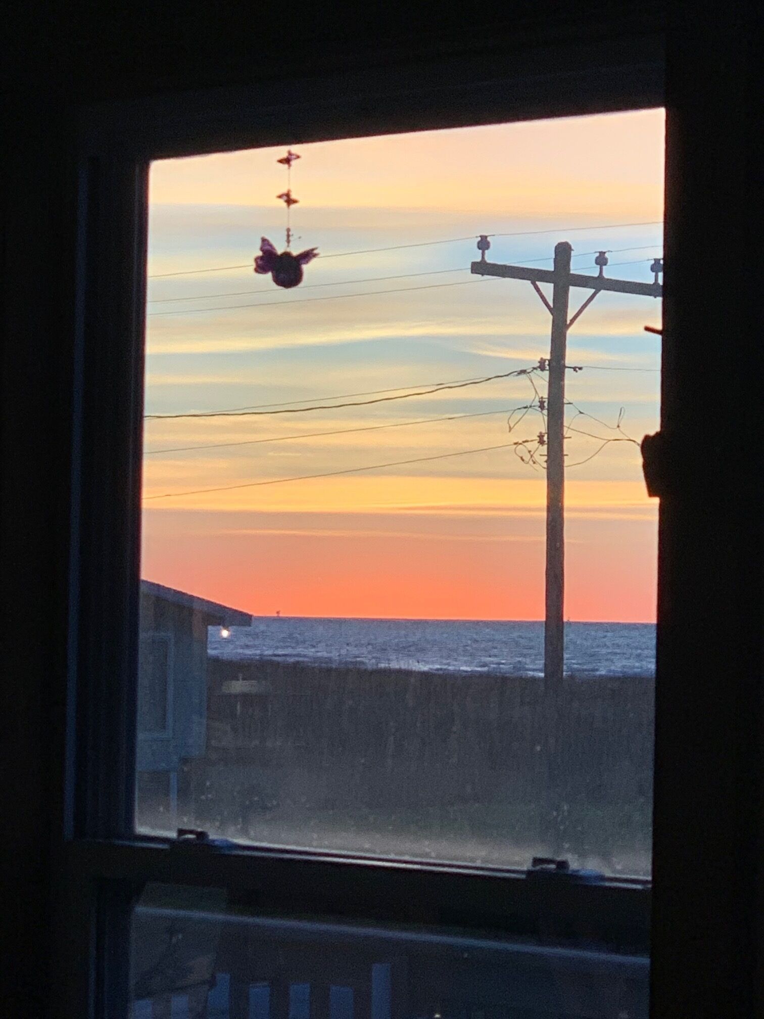 A sunset view through a window, featuring a power line and a building in the foreground.