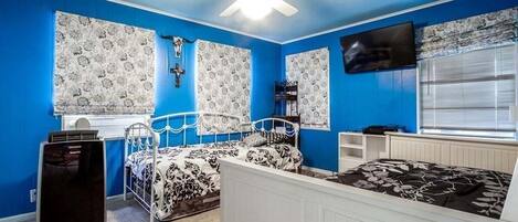 Un dormitorio con cama, ventilador de techo, televisión y cortinas estampadas.