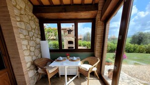 Une terrasse accueillante avec des murs en pierre, une table blanche agrémentée de deux chaises, et une vue sur un bâtiment en pierre et la verdure environnante.