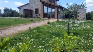 Une maison en pierre dotée d’un porche abrité, entourée d’un jardin où poussent des fleurs blanches.