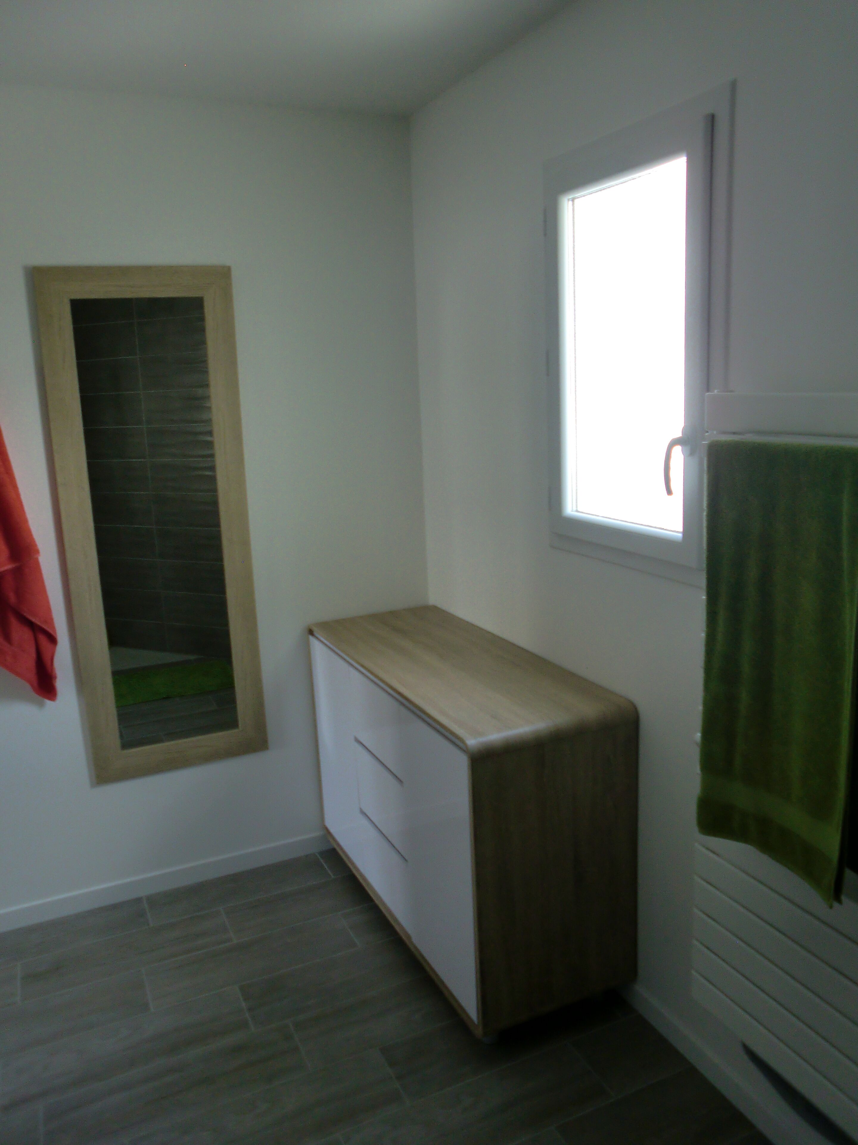 Un baño pequeño y limpio con un tocador de madera, una ventana y un perchero para toallas.