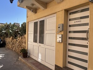 A building with two doors, one with a keypad and the other with a sign reading "All Nations Holiday Home." - All Nations Holiday Home (Ghajnsielem)