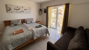 A bedroom with a bed, a nightstand, a window with curtains, and a view of the outside balcony. - All Nations Holiday Home (Ghajnsielem)