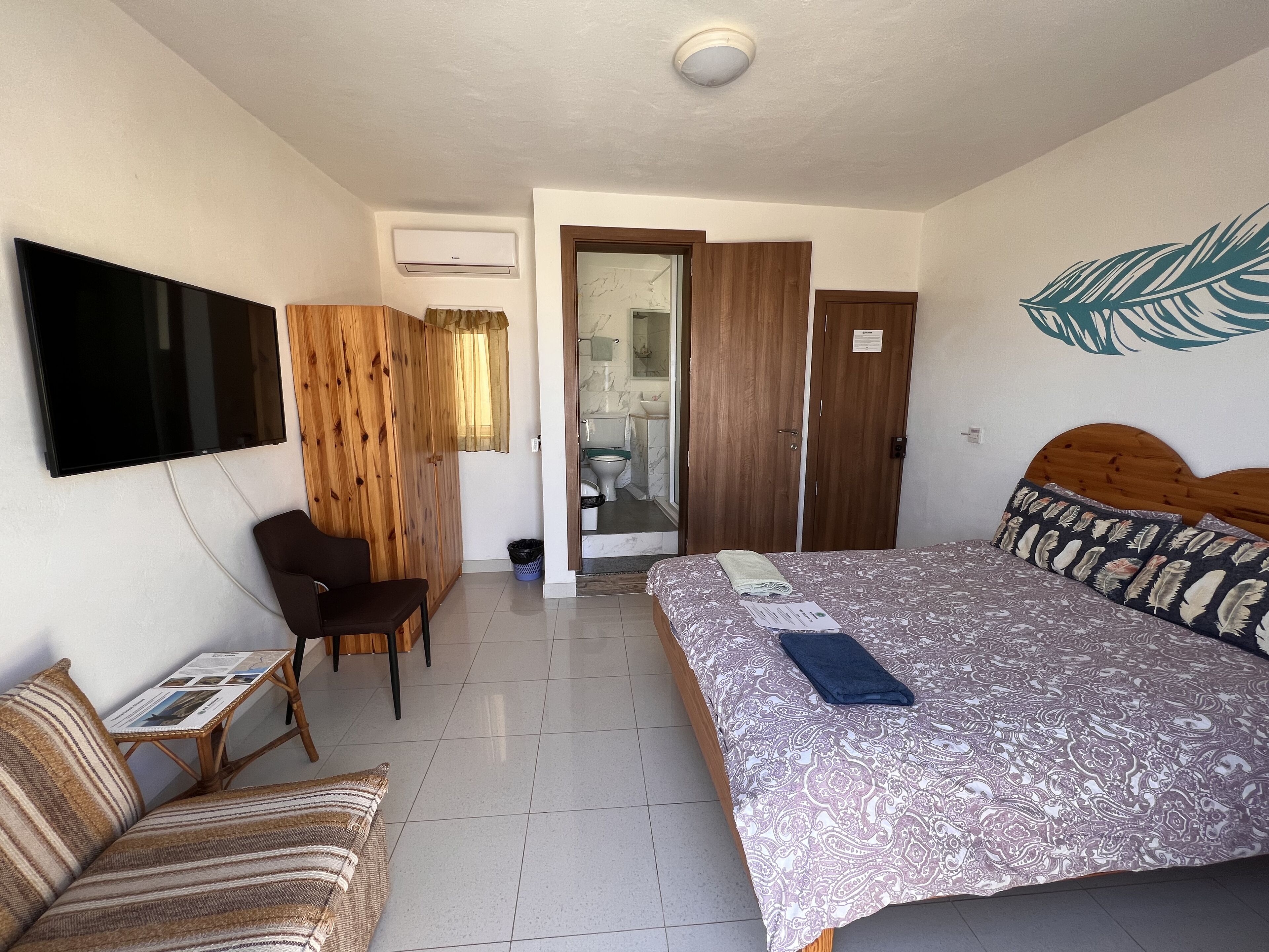 Une chambre d’hôtel avec un lit, une télévision, un bureau, une chaise et une salle de bain visible à travers une porte ouverte.
